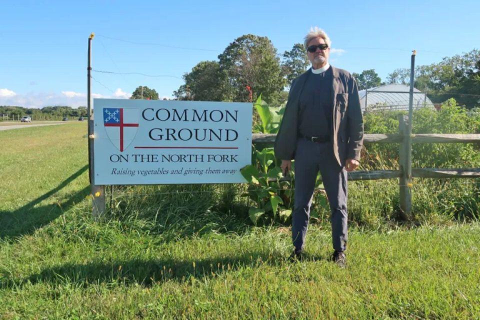 Roger Joslin stands in front of a sign that says "Common Ground Garden" with the garden in the background